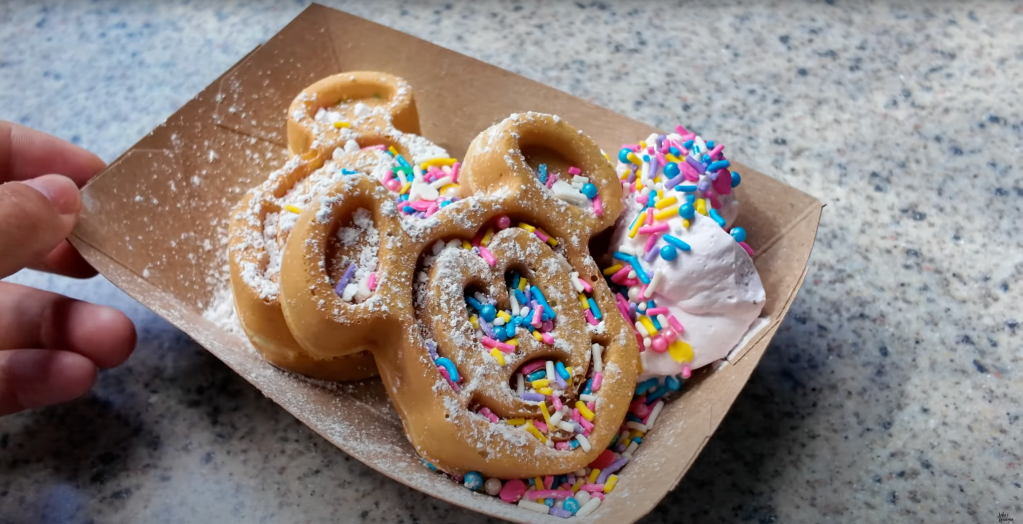 Disneyland 70th Anniversary Food, Disneyland Snacks, 70th Celebration Snacks, Disneyland Food Review, Disneyland 70th Anniversary Treats, Café Daisy Chicken Bacon Ranch Flop-Over, 70th Celebration Churro, Jolly Holiday Bakery Café Celebration Matterhorn Macaroon, Market House Mickey Hat Cookie, Red Rose Tavern 70th Stuff, 70th Celebration Macaron, Refreshment Corner Pulled Pork Mac and Cheese in a Bread Bowl, Tiana’s Palace House-filled Celebration Beignet, Troubadour Tavern W.E.D. Chili Cheese Baked Potato, Troubadour Tavern Chicken Pot Pie Baked Potato, Troubadour Tavern Tiramisu Cold Brew, Hollywood Lounge Celebration Cocktail, Hollywood Lounge Pink Dragon Fruit Mimosa, Schmoozies Mickey-shaped Celebration Waffles, Disneyland Celebration Snacks 2023, Disneyland Food Guide, Disneyland Special Drinks, Disneyland Bakery Items, Disneyland Menu Highlights, Disneyland Sweet Treats, Disneyland Savory Snacks, Disneyland Party Foods, Disneyland Anniversary Eats